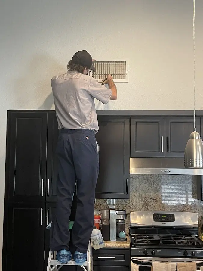 Technician inspecting an air vent during HVAC service in Adelanto